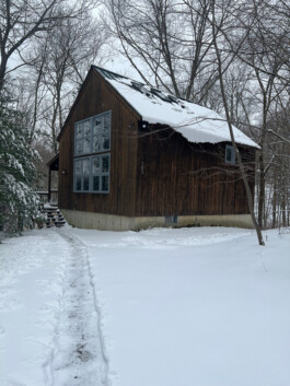 A colour photograph of one of the studios at the Josef & Anni Albers Foundation, Bethany, Connecticut, where Henry Ward undertook a residency in 2023. It shows a wooden cabin in the woods surrounded by snow. Anomie Publishing